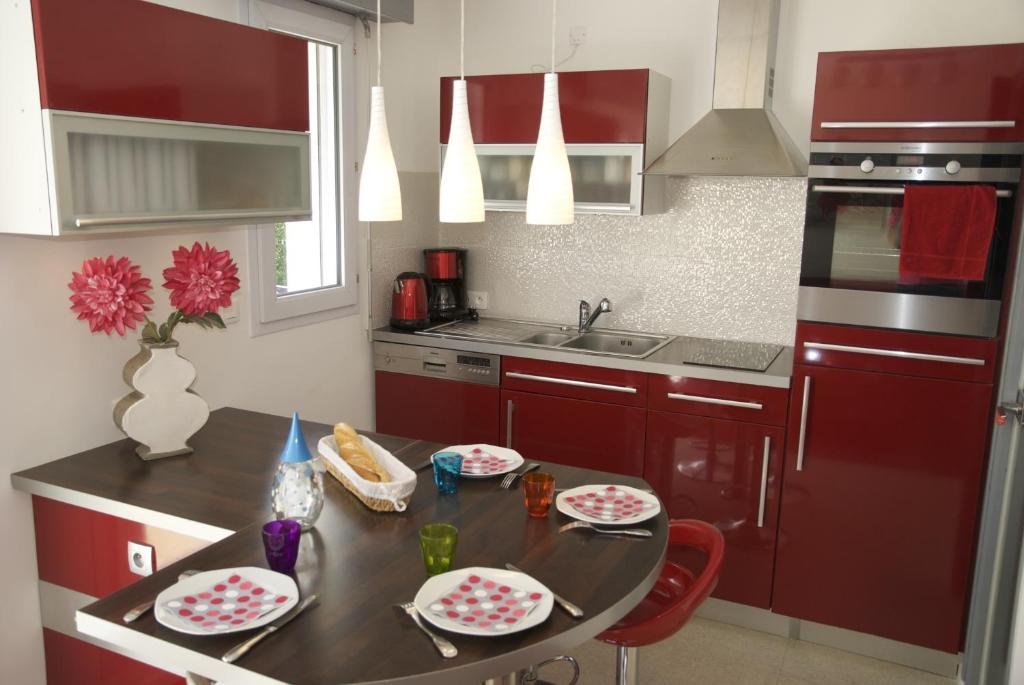 Gîte La Terrasse Du Verger في كاركفو: مطبخ به دواليب حمراء وطاولة عليها صحون