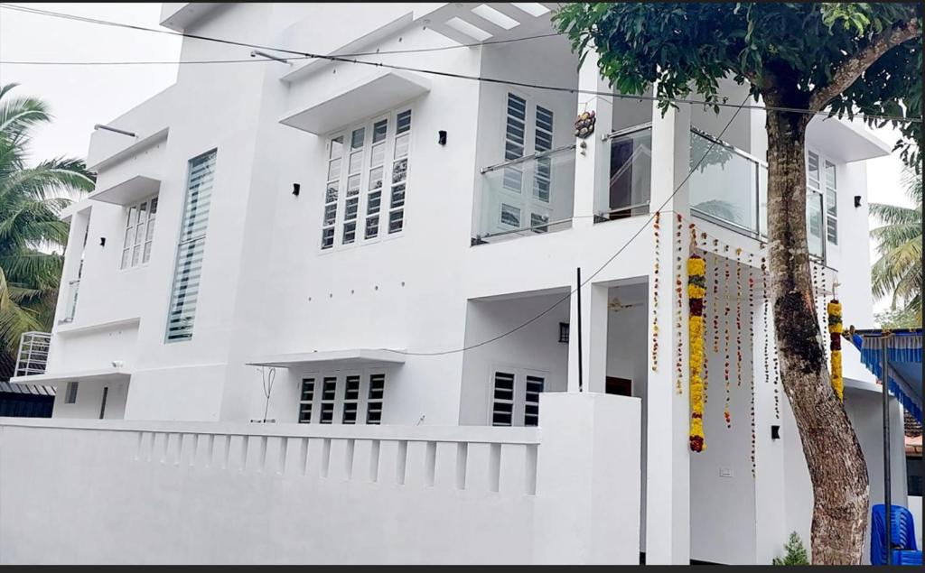 a white building with a tree in front of it at Rohini Homestay 3Bhk AC - House boat Available in Alleppey