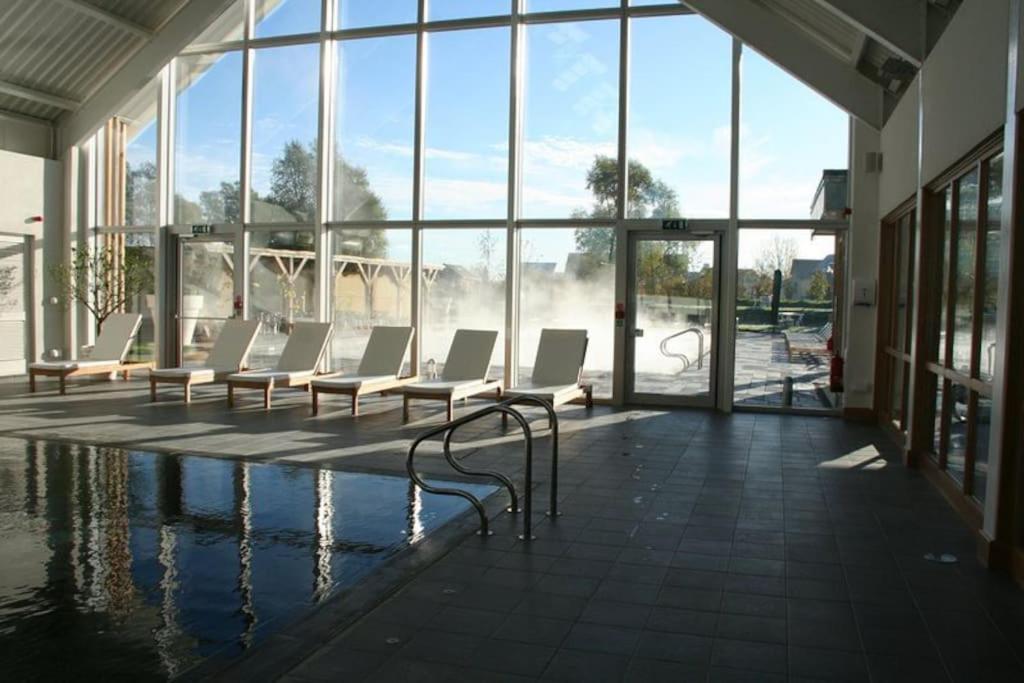 a pool with white chairs in a building with windows at Blueberry Cottage - Lower Mill Estate in Somerford Keynes