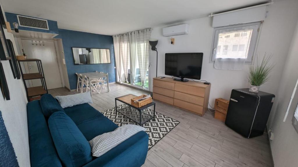 ein Wohnzimmer mit einem blauen Sofa und einem TV in der Unterkunft Charmant 2p, piscine, clim, à 5 min de la plage in Vallauris