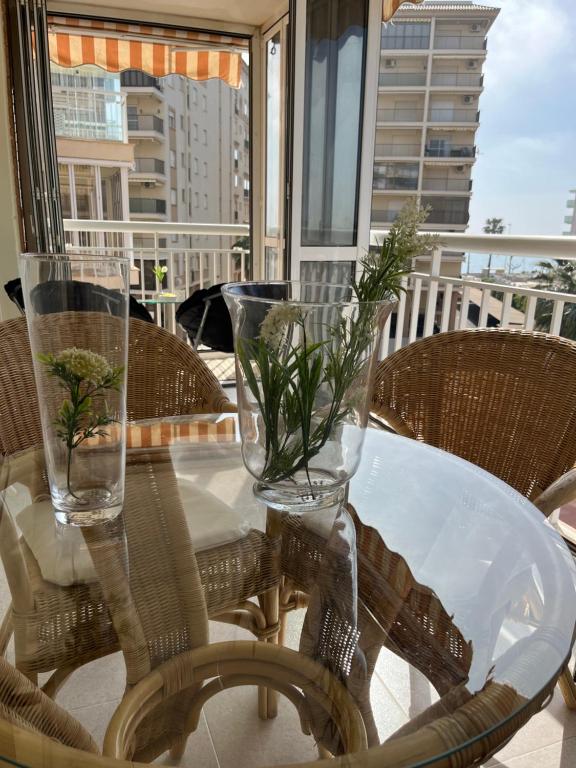 einen Glastisch mit Blumen in Vasen auf dem Balkon in der Unterkunft Apartamento a pie de playa con vistas al mar y piscina in Benicàssim
