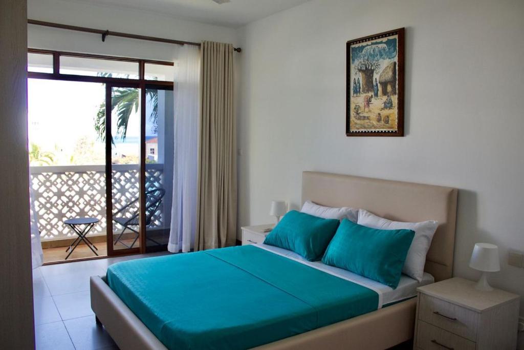 Schlafzimmer mit einem Bett mit blauer Bettwäsche und einem Balkon in der Unterkunft TAUSI HOMES Sultan Palace Beach Resort in Kilifi