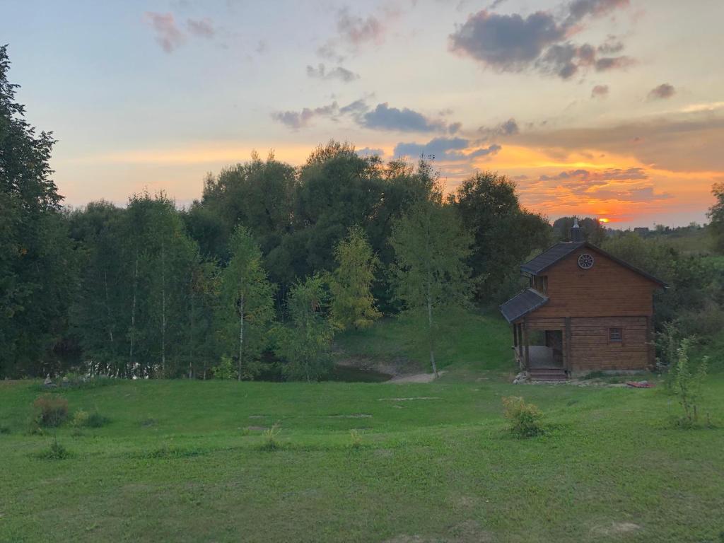 una pequeña casa en un campo con una puesta de sol en el fondo en Liepų pirtis, en Miežoniai