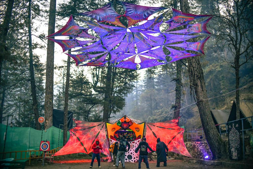 a group of people flying kites in a forest at Himtrek Riverside Camps, Kasol in Kasol