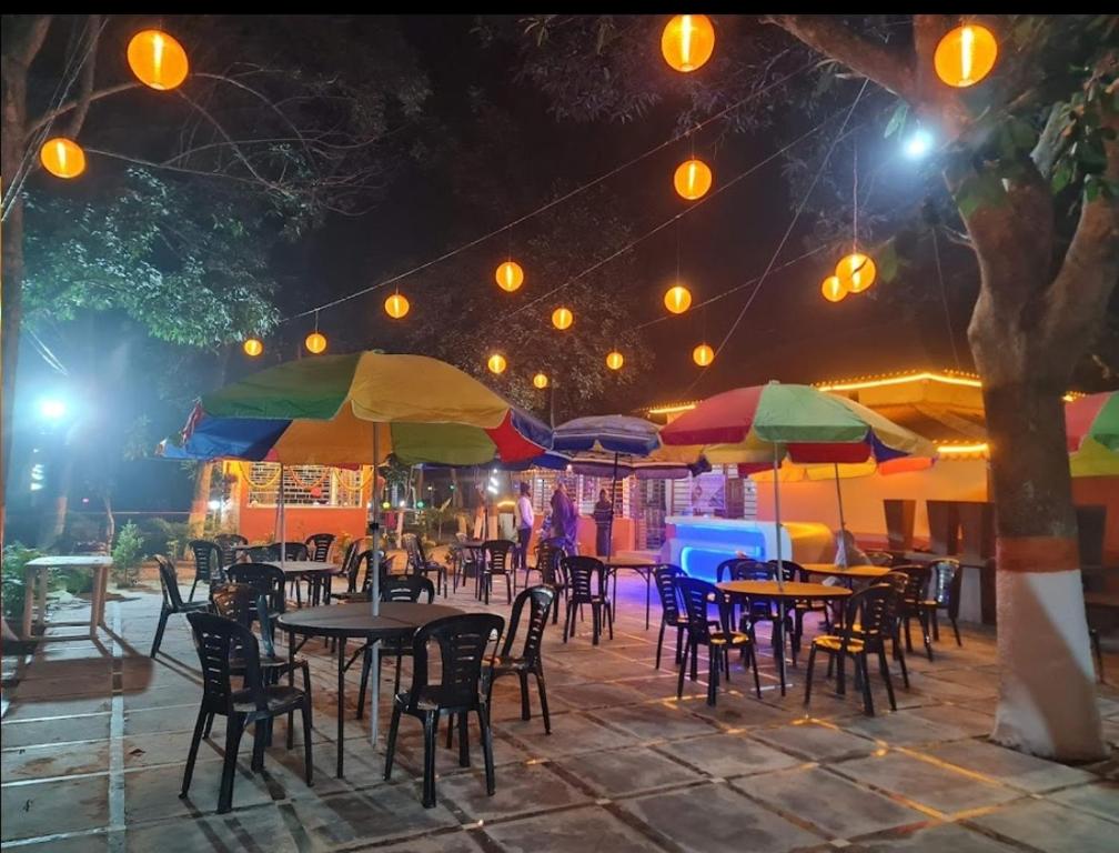 eine Terrasse mit Tischen, Stühlen und Sonnenschirmen in der Nacht in der Unterkunft Basundhara Resort Cum Family Restaurant in Kharagpur