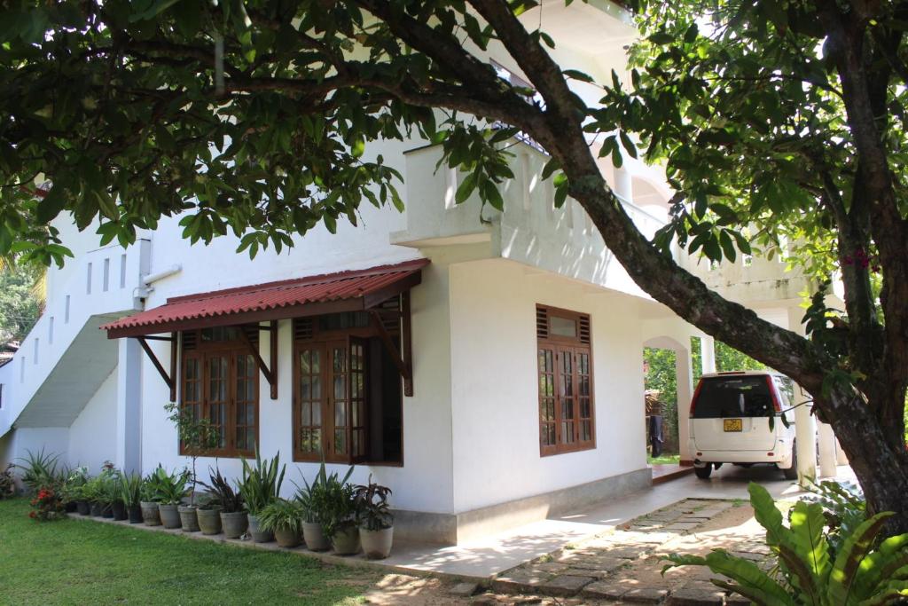 une maison blanche avec un arbre devant dans l'établissement The Dalawella Porch House, à Galle