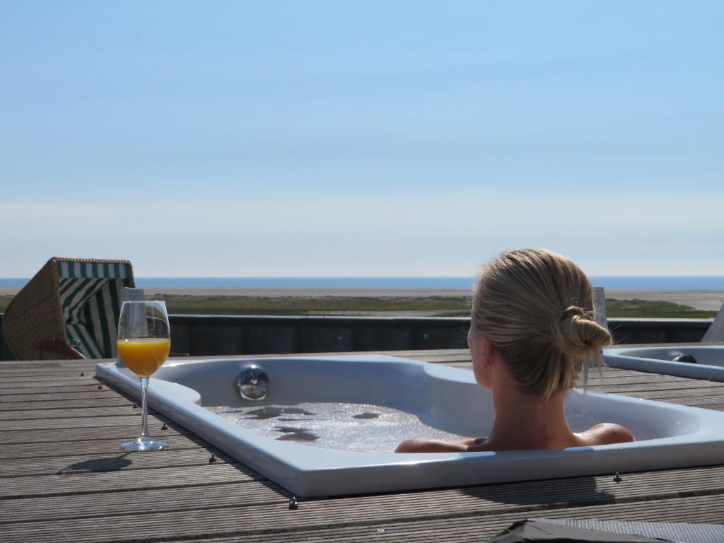 une femme assise dans une baignoire avec un verre de vin dans l'établissement ambassador hotel & spa, à Sankt Peter-Ording
