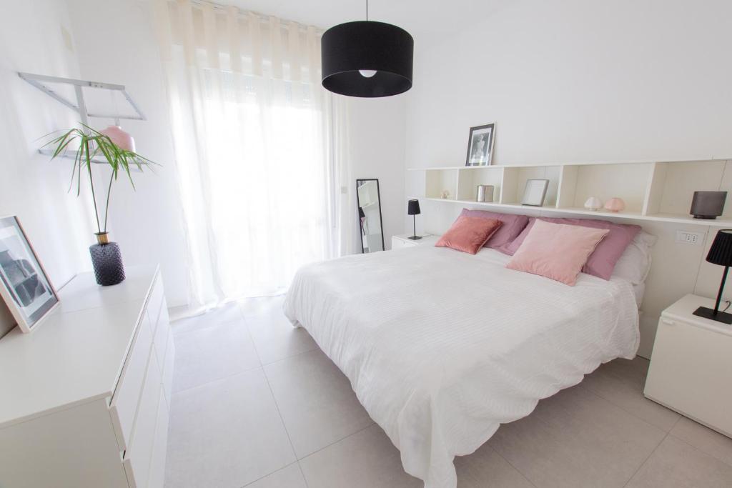 een witte slaapkamer met een groot wit bed met roze kussens bij VIRGINIA APPARTAMENTI RICCIONE in Riccione
