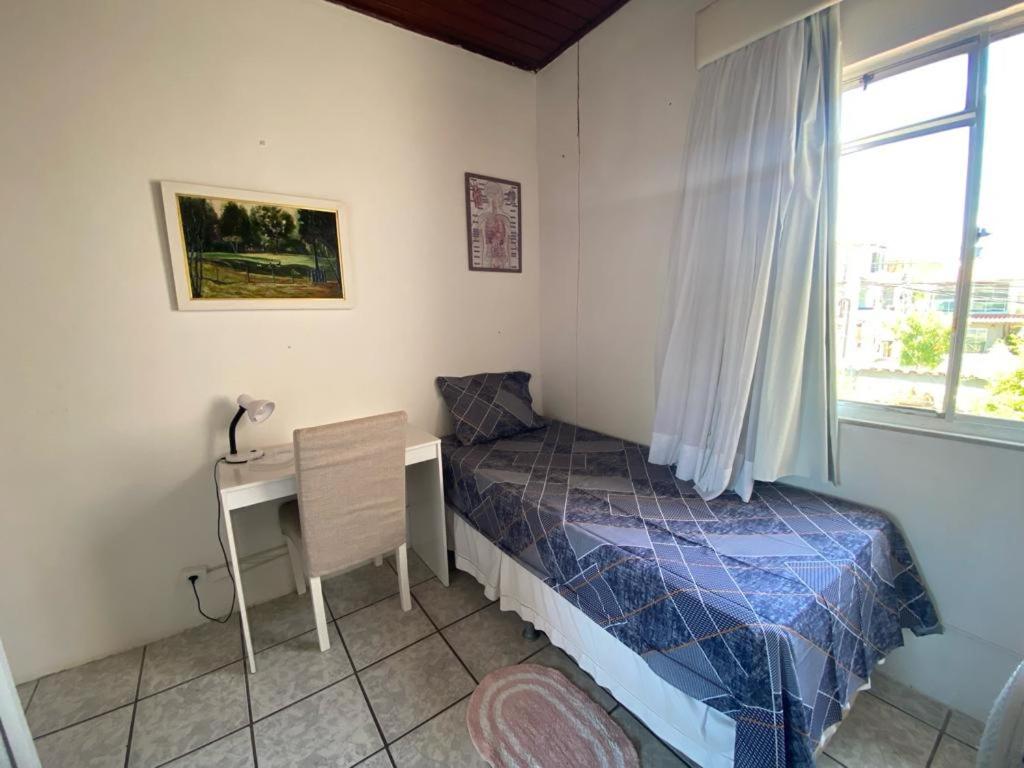 a bedroom with a bed and a desk and a window at Quarto em stella maris in Salvador