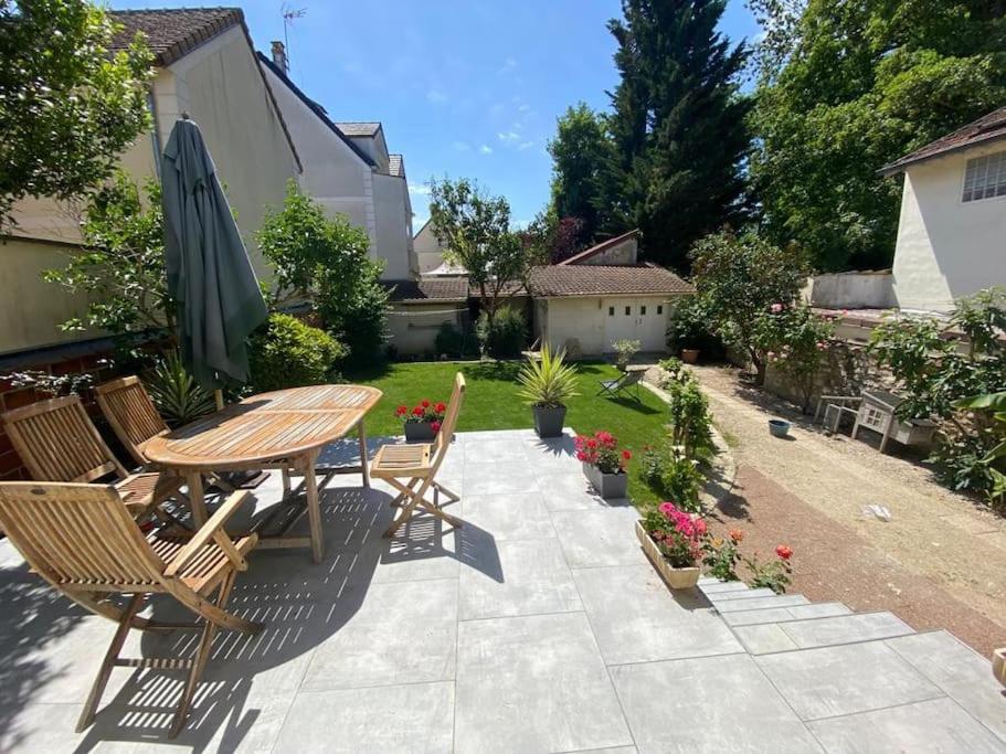 un patio avec une table, des chaises et un parasol dans l'établissement Maison lumineuse avec jardin, proche Paris Disney et Paris, à Lagny-sur-Marne