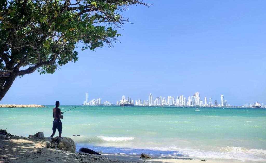 a man standing on a beach with a city in the background at La Caracola Cartagena in Cartagena de Indias