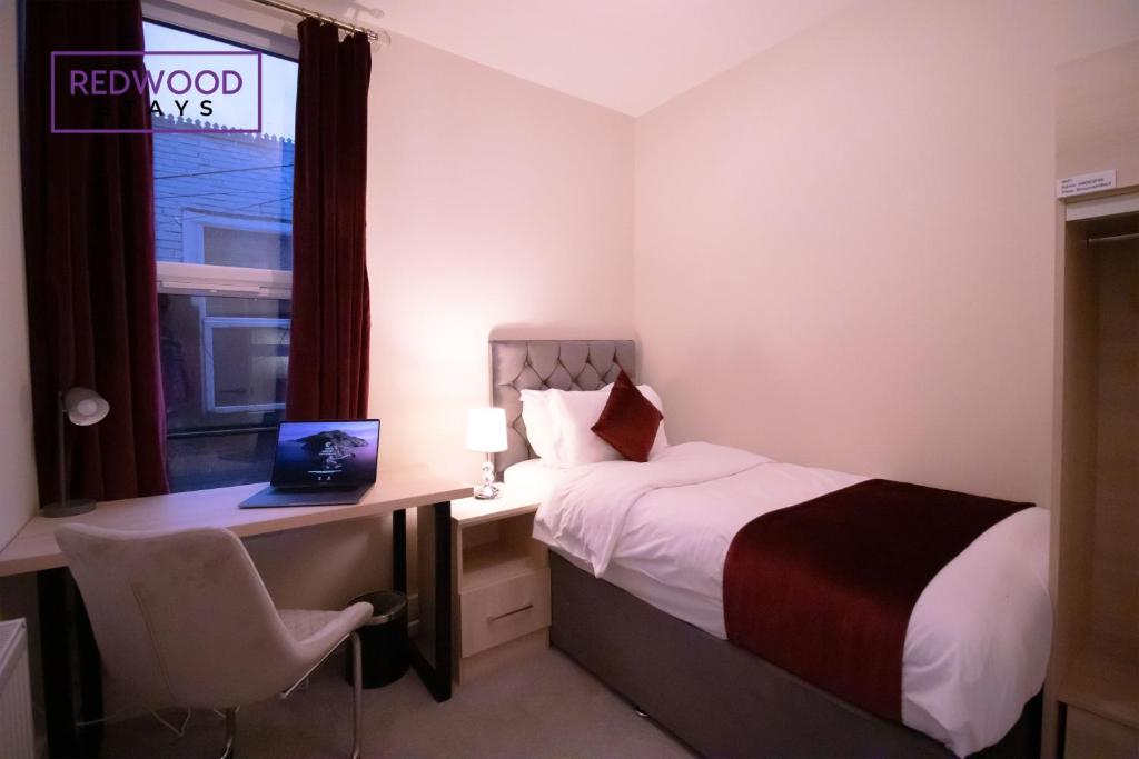 a hotel room with a bed and a desk with a laptop at Everest Lodge Serviced Apartments for Contractors & Families, FREE WiFi & Netflix by REDWOOD STAYS in Farnborough