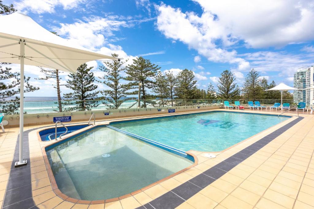 a swimming pool at a resort with an umbrella at Beachfront 2-Bed with Pool, BBQ & Tennis Court in Gold Coast