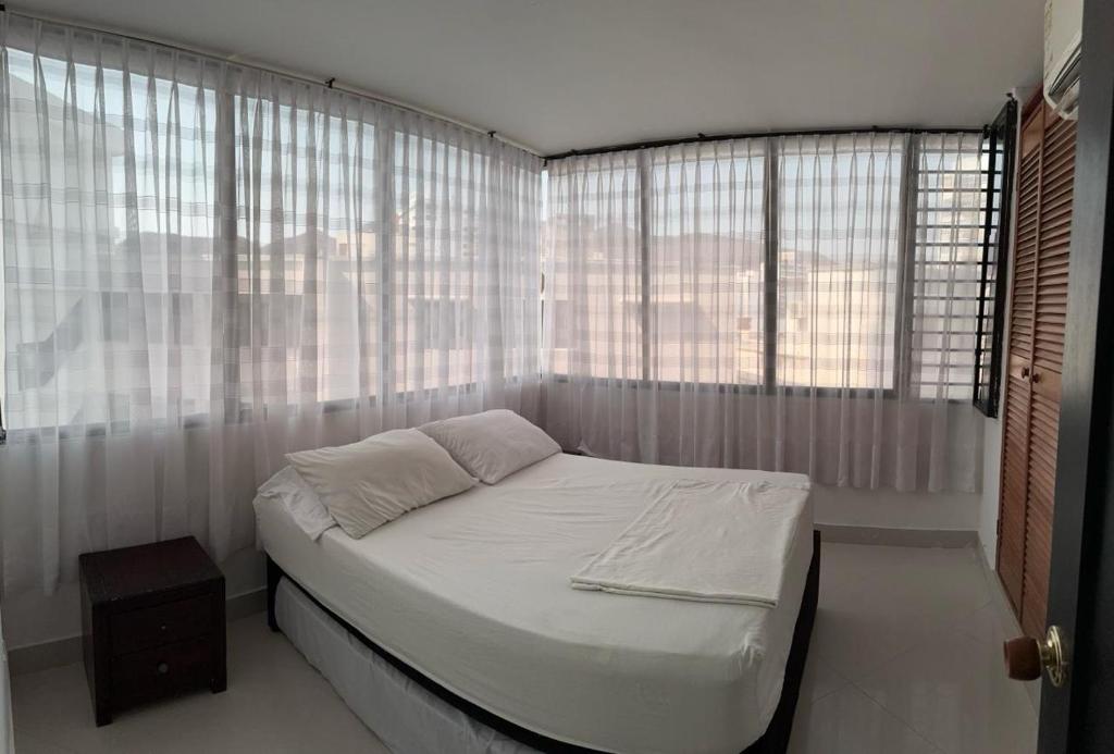 Cama en habitación con ventanas y sábanas blancas en Encantador apto en el Rodadero frente a la playa, en Santa Marta