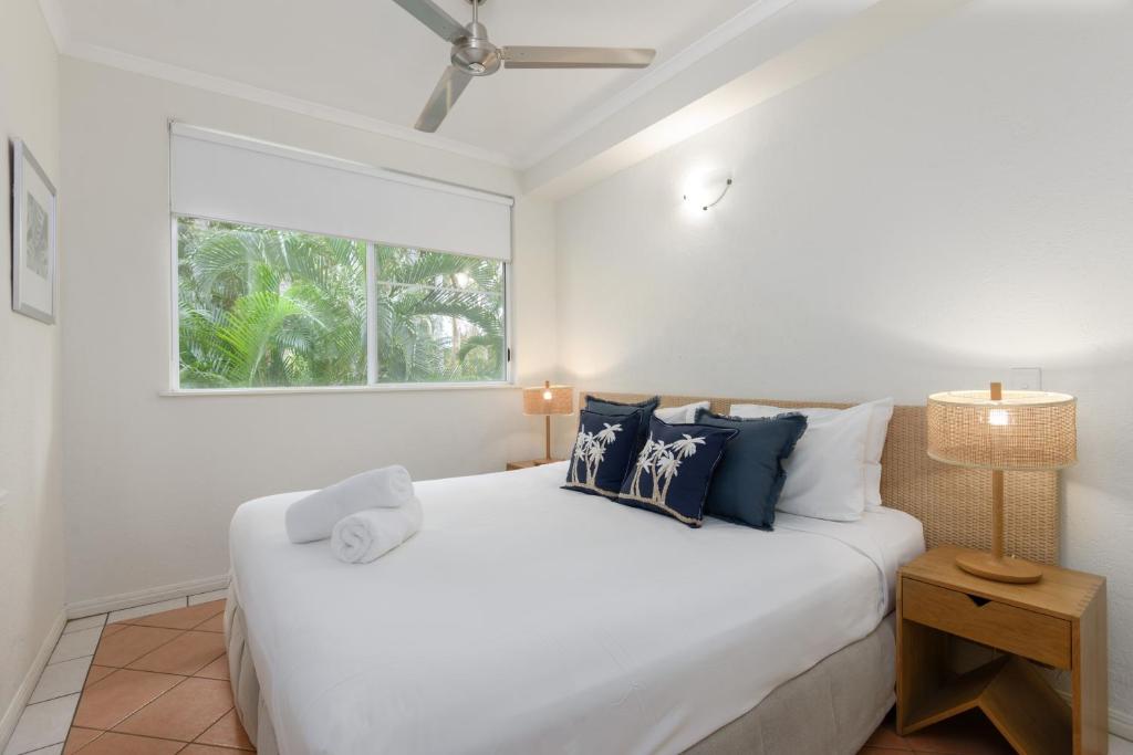 a white bedroom with a large bed and a window at Coral Apartments Port Douglas in Port Douglas