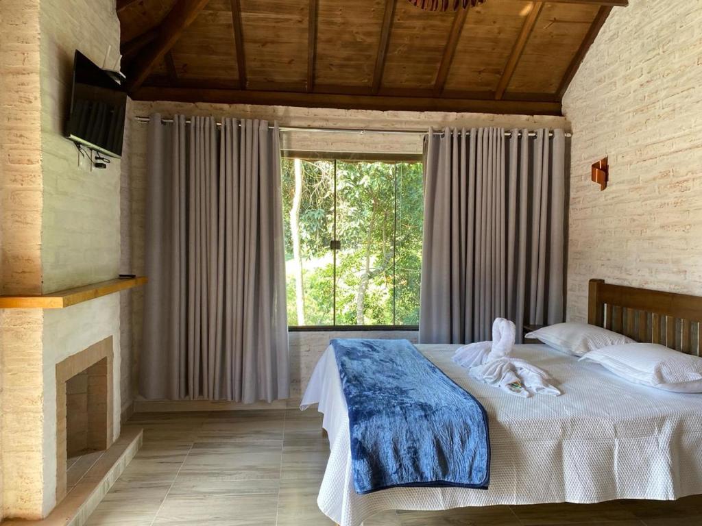 a bedroom with a bed and a large window at Chales Bela Serra in Monte Verde