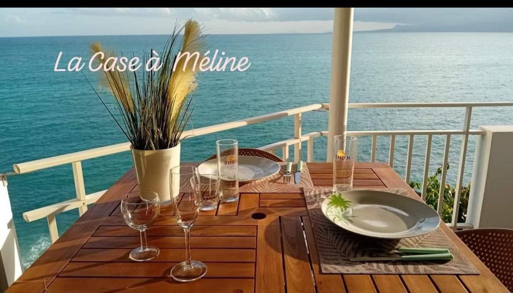 a wooden table with wine glasses and the ocean at La Case à Méline in Le Gosier