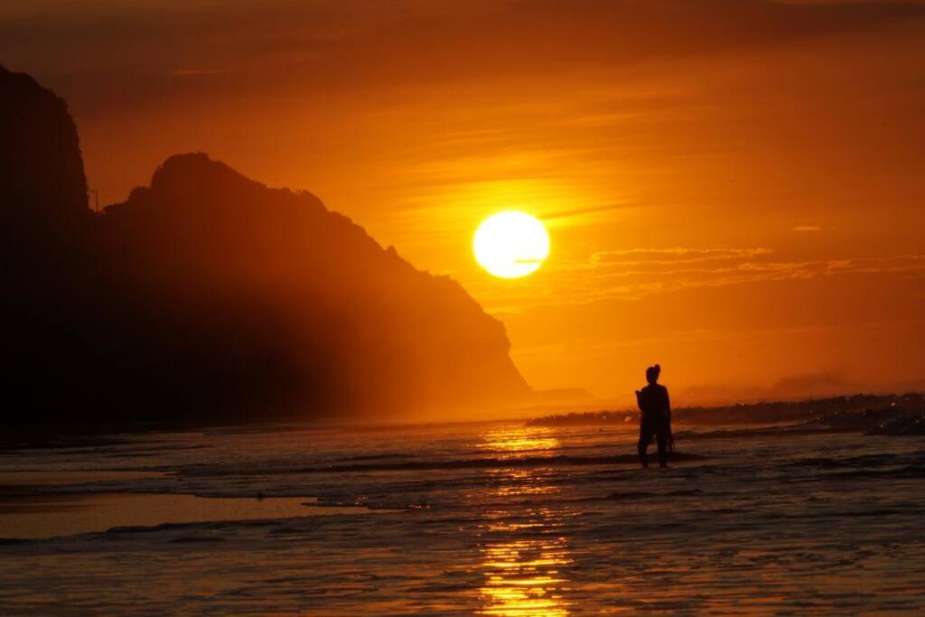 un hombre de pie en el océano viendo la puesta de sol en Casa BLUE paradise HOUSE, en El Corozal