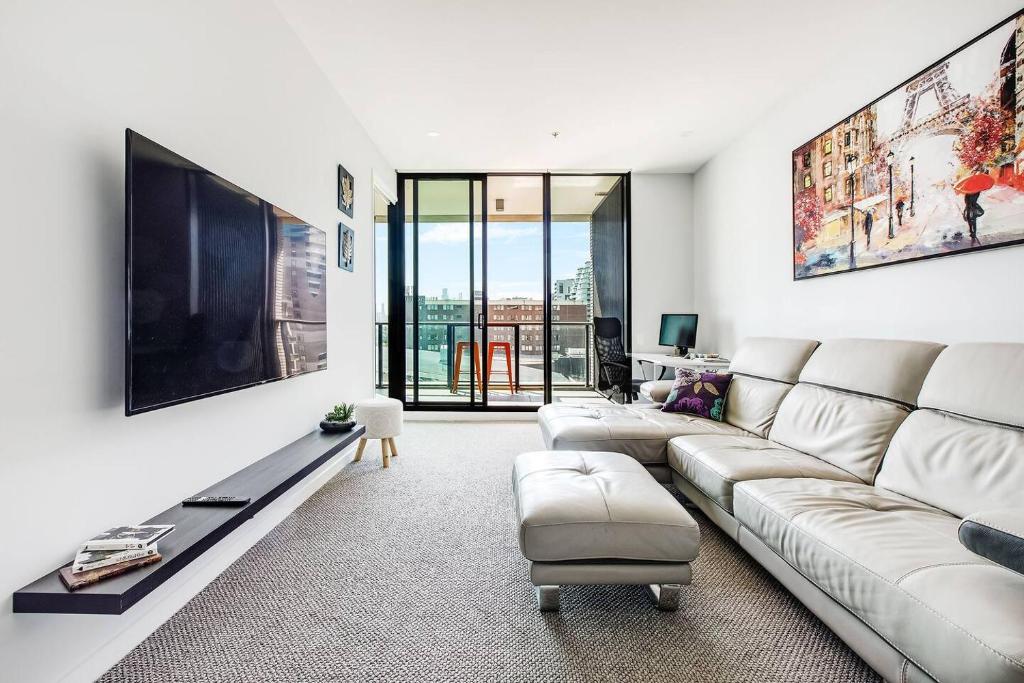 ein weißes Wohnzimmer mit einem Sofa und einem TV in der Unterkunft Queens Corner - Lakeside Serenity at Albert Park in Melbourne