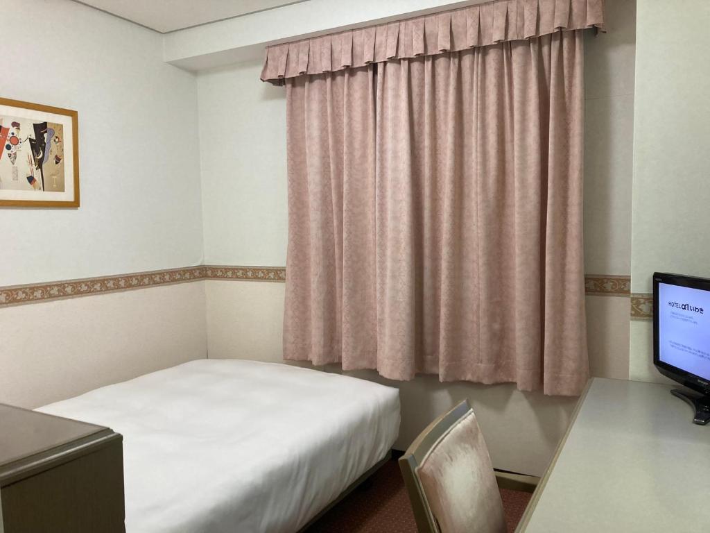 a small room with a bed and a desk and a window at Hotel Alpha-One Iwaki in Iwaki