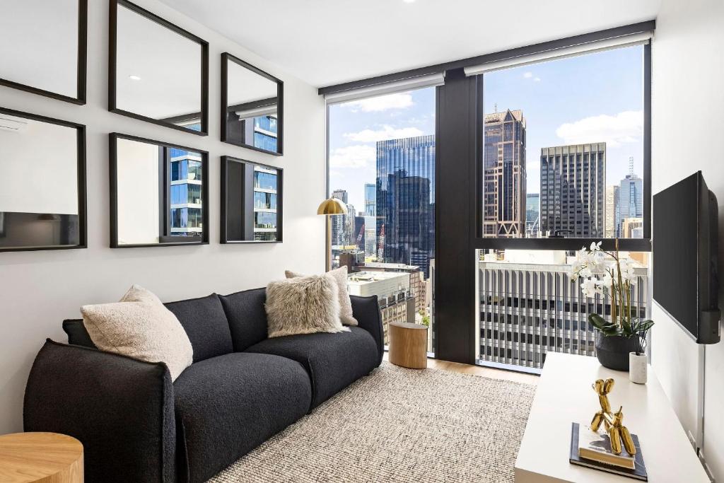 sala de estar con sofá y ventanas grandes en Luxuria Apartments - Collins House en Melbourne