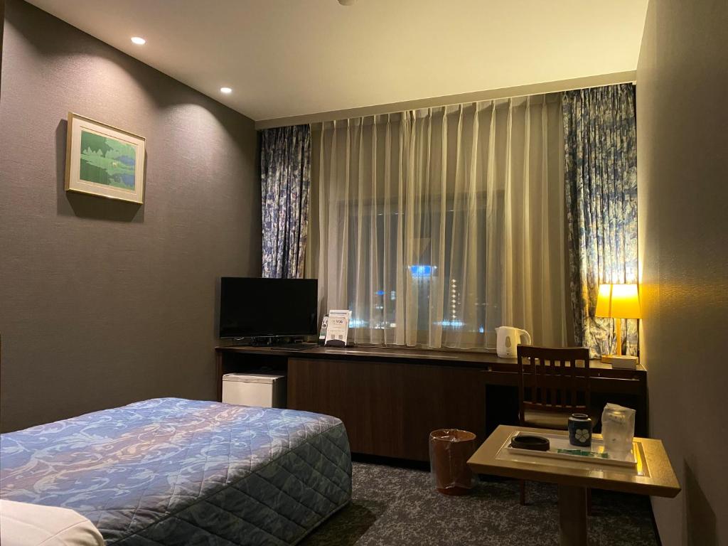近江八幡市にある近江八幡ステーションホテルのベッド、デスク、窓が備わるホテルルームです。