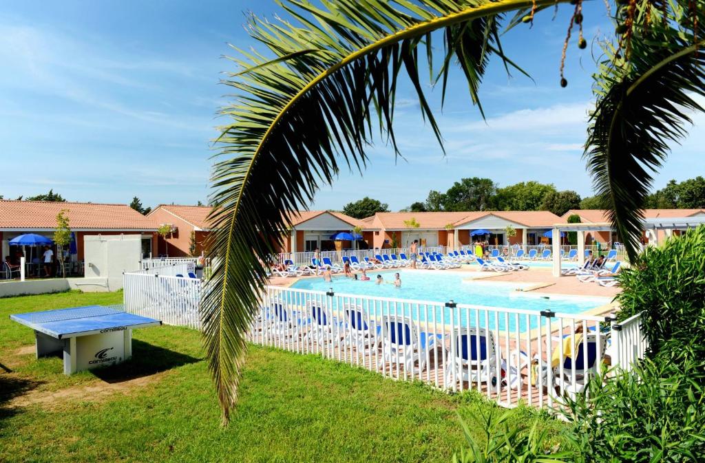 een zwembad in een resort met een tafel en een palmboom bij Résidence Odalys Côté Canal in Sallèles-dʼAude