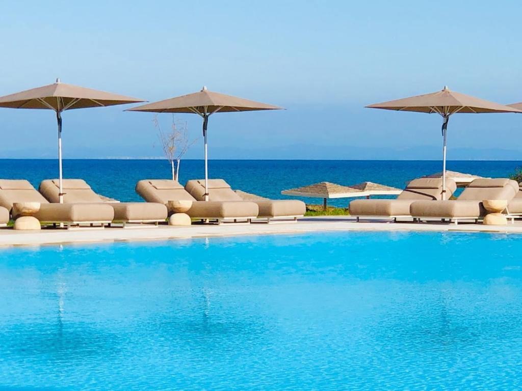 a swimming pool with chairs and umbrellas and the ocean at The Bay Hotel & Suites in Vasilikos
