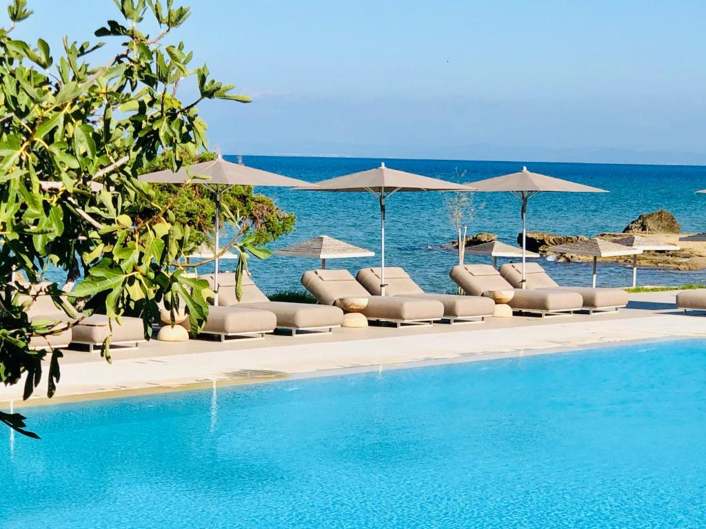 a pool with lounge chairs and umbrellas and the ocean at The Bay Hotel & Suites in Vasilikos