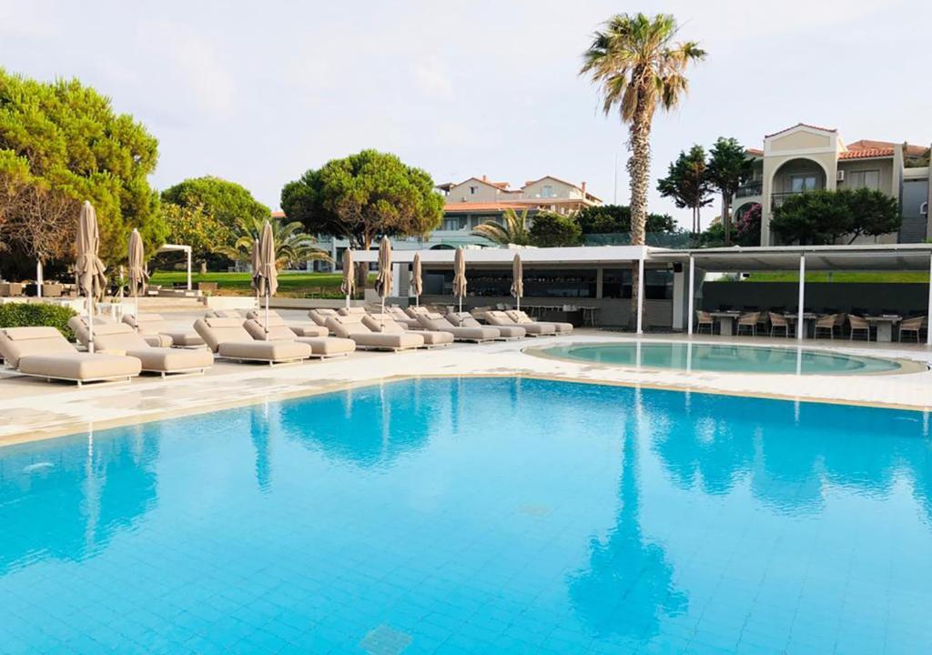 a swimming pool with lounge chairs and a palm tree at The Bay Hotel & Suites in Vasilikos