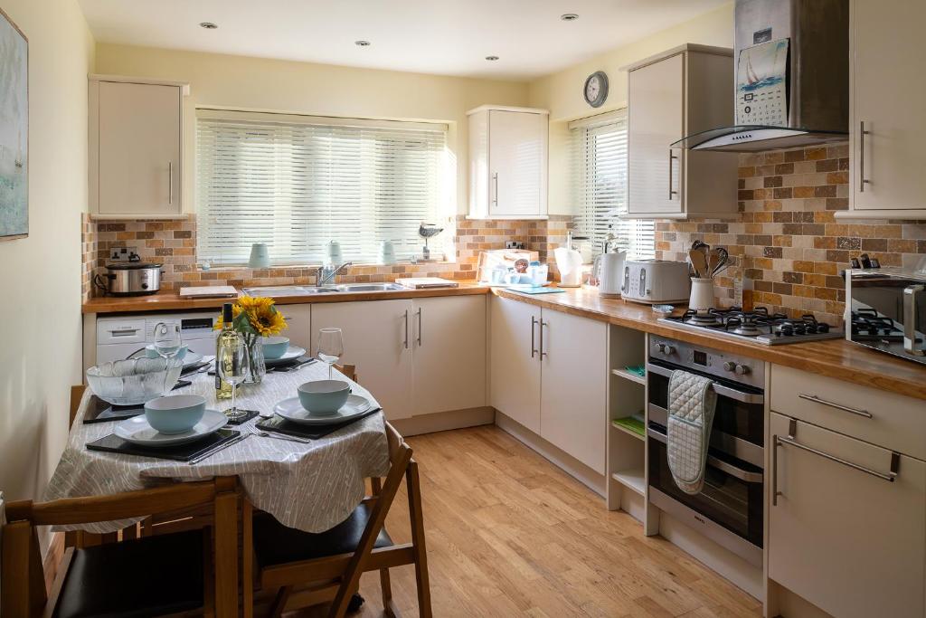 una cocina con armarios blancos y una mesa con sillas. en Orme View en Llanfairfechan