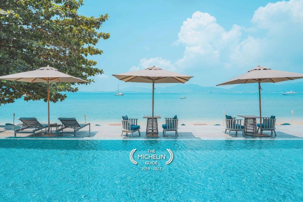 a pool with chairs and umbrellas next to the ocean at My Beach Resort Phuket in Panwa Beach