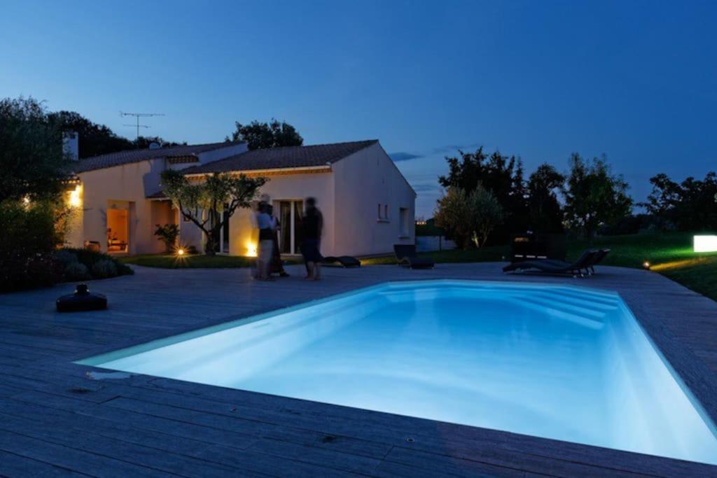 two people standing next to a swimming pool at night at la villa d'Ariane-piscine-jaccuzi-15 mn Mer in Vendargues