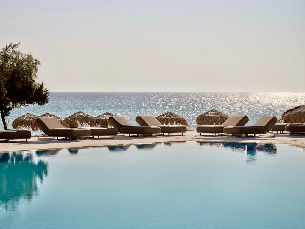 uma piscina com cadeiras e o oceano ao fundo em The Bay Hotel & Suites em Vasilikos