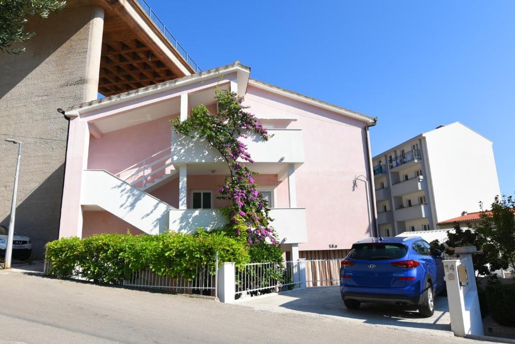 une voiture bleue garée devant un bâtiment rose dans l'établissement Apartments Vodanović, à Podgora