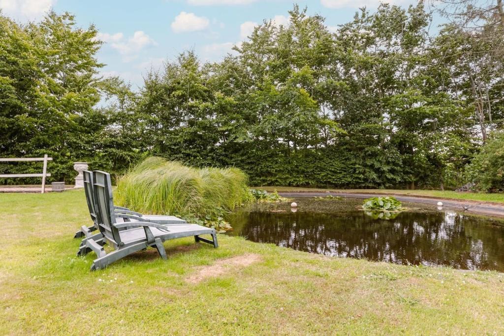 un banco sentado en el césped junto a un estanque en Farmhouse oasis with garden, pond and idyllic surroundings en Beernem