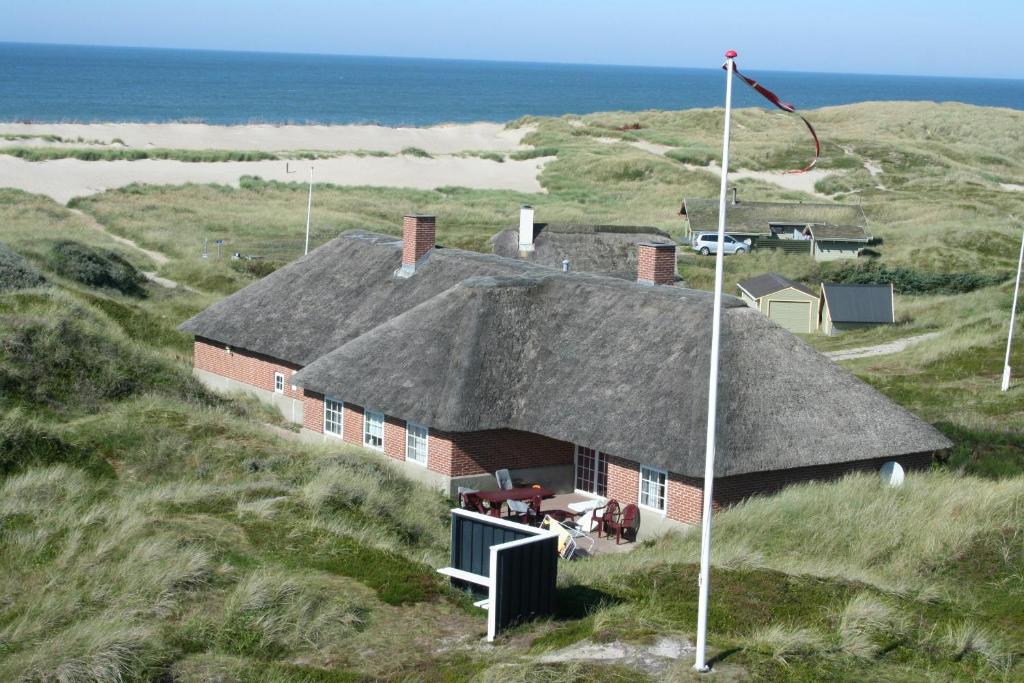 uma casa com um telhado de palha no topo de um campo em Thatched house with pool by the sea - SJ690 em Harboør