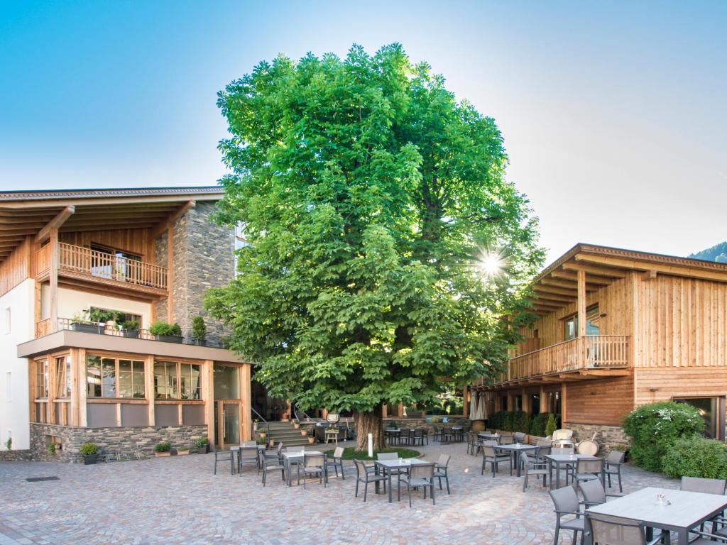 un arbre avec des tables et des chaises devant un bâtiment dans l'établissement Hotel Gasthof Höllriegl, à Sarentino