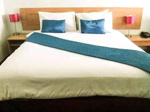 a large white bed with blue pillows on it at Brakendene Lodge in Gaborone