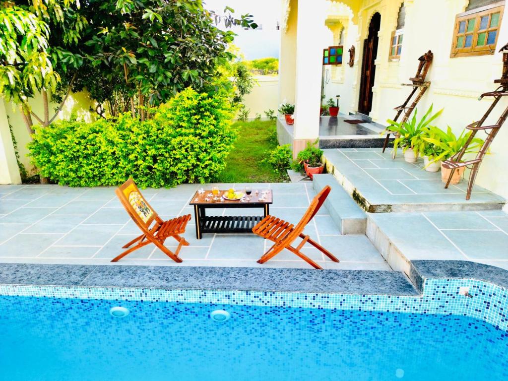 un patio con 2 sillas y una mesa junto a la piscina en The heavens villa, en Udaipur
