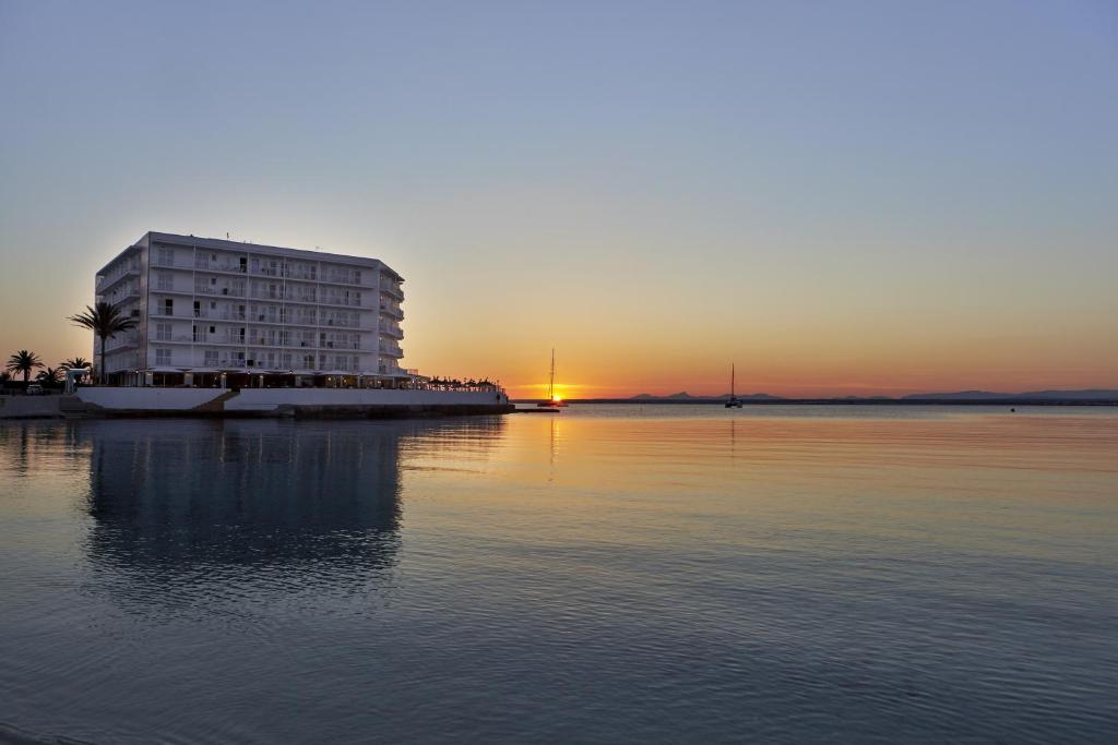 a building on the water with the sunset in the background at Universal Hotel Marqués in Colònia de Sant Jordi