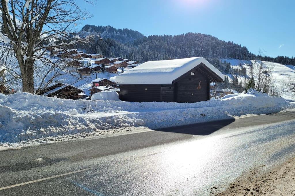 a house is covered in snow next to a road at Le Petit Chalet du Chinaillon in Le Grand-Bornand