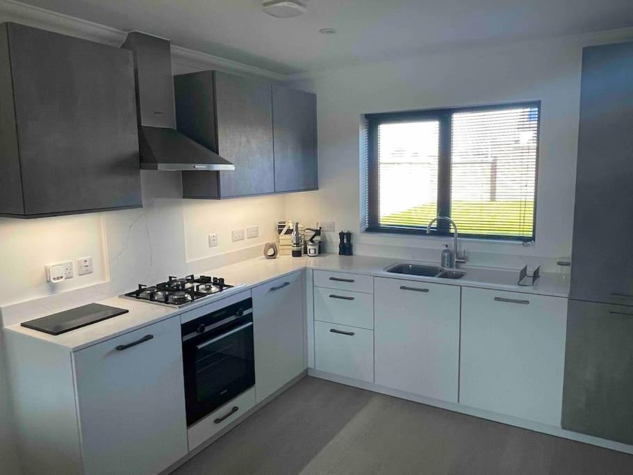 Modern 2 Bedroom House, Edinburgh. في Millerhill: مطبخ بدولاب بيضاء وفرن علوي موقد