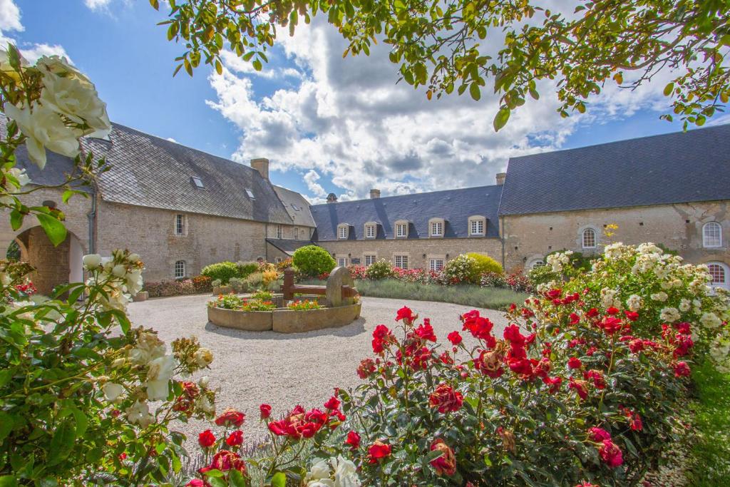 um jardim com flores vermelhas em frente a um edifício em Ferme de la Rançonnière - Hôtel & Restaurant em Crépon