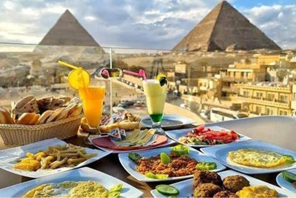 Carpet Alaadein Pyramids view في القاهرة: طاوله مع اطباق طعام واهرامات