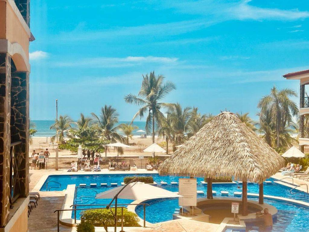 um resort com uma piscina e um guarda-sol de palha em Apartamento de lujo frente a playa Jacó-3 BD/ 2 BA em Jacó