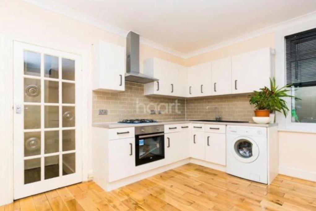 eine Küche mit weißen Schränken, einer Waschmaschine und einem Trockner in der Unterkunft 1 bedroom ground floor flat in Greenford