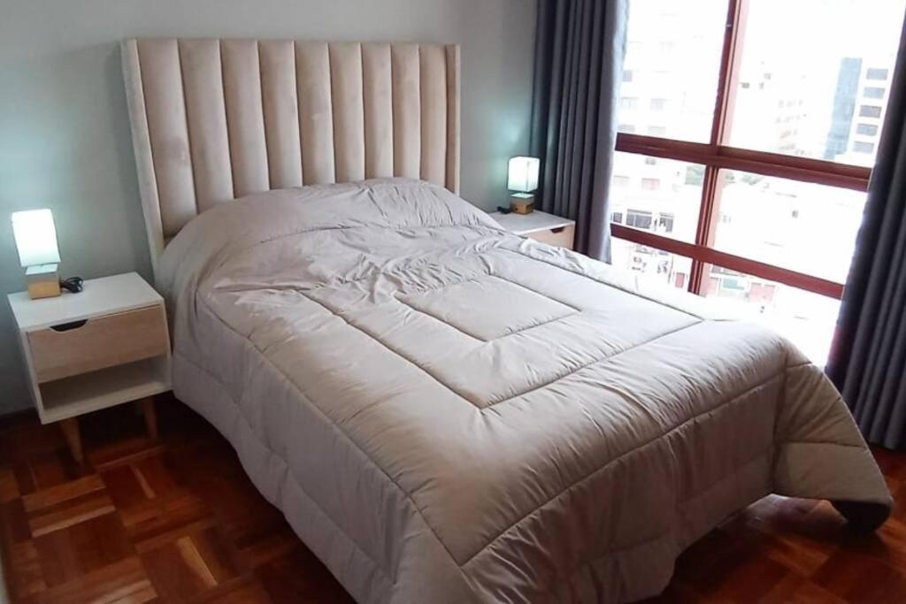 a white bed in a bedroom with a large window at Estudio a estrenar en Miraflores in La Paz