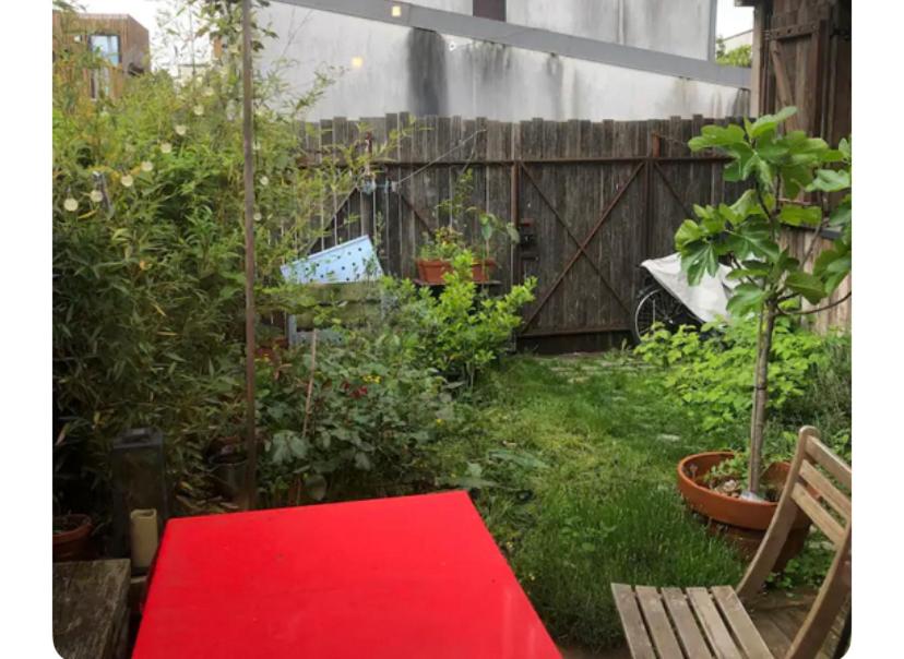 einen Garten mit einem roten Tisch und einem Zaun in der Unterkunft Maison avec terrasse-jardin proche métro in Montreuil