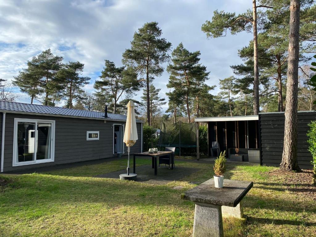 een achtertuin met een huis en een tafel en een paraplu bij Chalet de Bosrand 404, unieke rustige plek met veel privacy aan de bosrand van vakantiepark op de Veluwe in Beekbergen